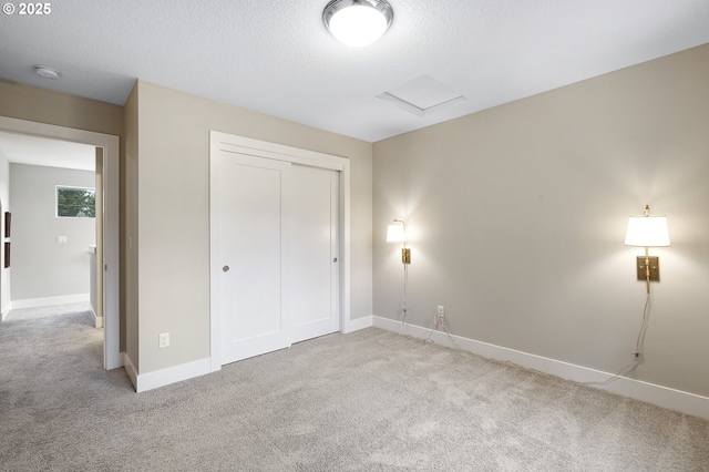 unfurnished bedroom featuring a textured ceiling, light colored carpet, baseboards, a closet, and attic access