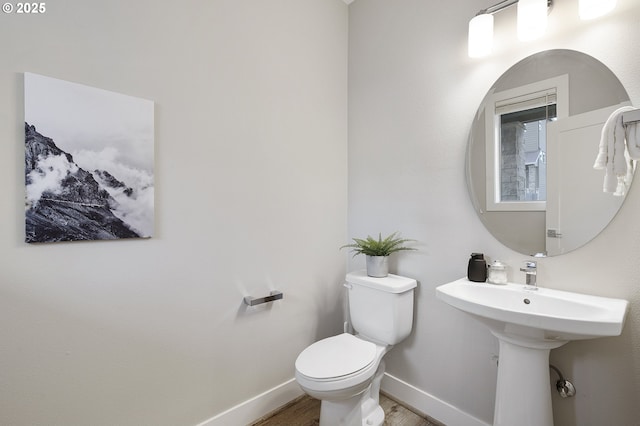 half bath with baseboards, toilet, and wood finished floors