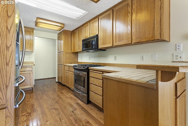 540 NE 23rd Pl, Gresham, OR 97030 - kitchen featuring appliances with stainless steel finishes, tile counters, dark wood-style floors, brown cabinets, and a textured ceiling