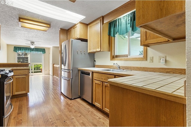 540 NE 23rd Pl, Gresham, OR 97030 - kitchen with stainless steel appliances, tile countertops, a textured ceiling, ceiling fan, and light wood-type flooring