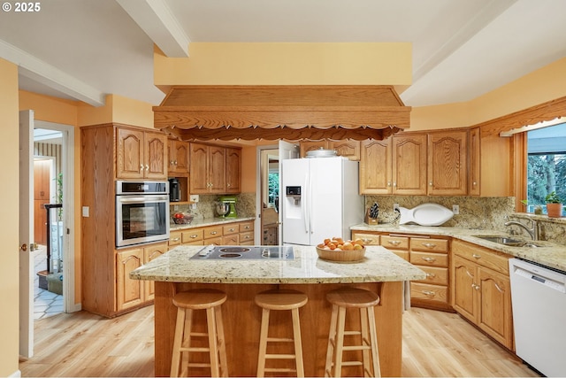 kitchen with a sink, light stone counters, backsplash, white appliances, and light wood-style floors