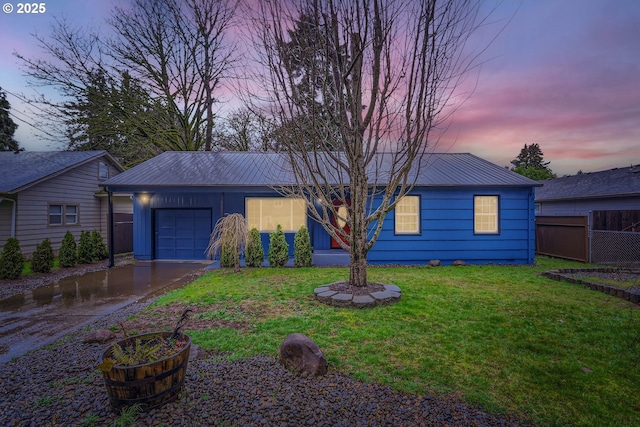 view of front facade with a yard, an attached garage, metal roof, fence, and driveway