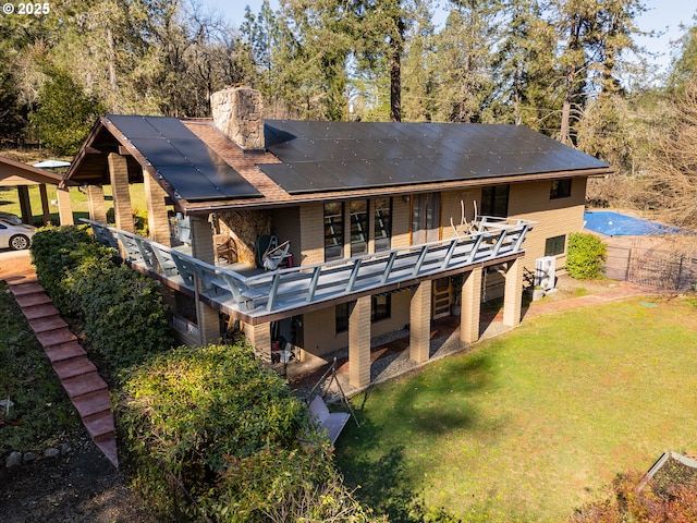 back of property featuring a wooden deck, a lawn, and solar panels