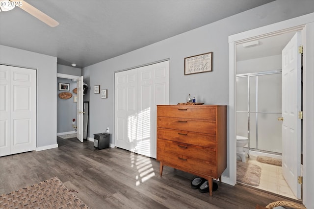 bedroom with dark wood-type flooring, two closets, connected bathroom, and baseboards