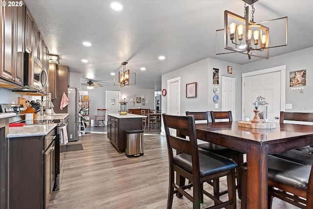 dining space featuring light wood-style flooring, ceiling fan with notable chandelier, a textured ceiling, and recessed lighting