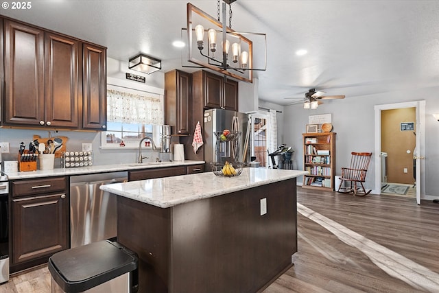 kitchen featuring a center island, hanging light fixtures, appliances with stainless steel finishes, dark brown cabinetry, and a sink