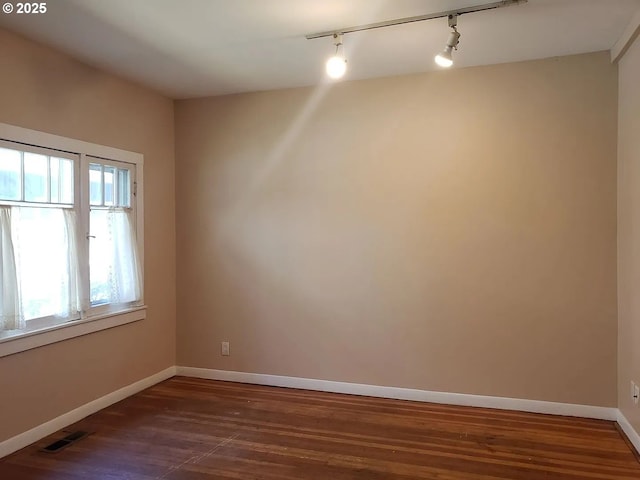 spare room with dark wood-type flooring, visible vents, and baseboards