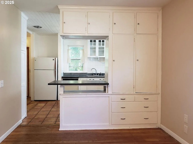 kitchen with backsplash, freestanding refrigerator, white cabinetry, a sink, and baseboards