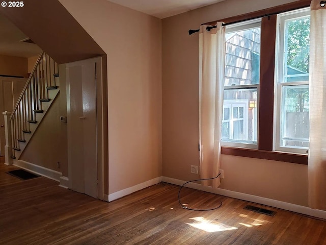 empty room featuring stairs, wood finished floors, visible vents, and baseboards