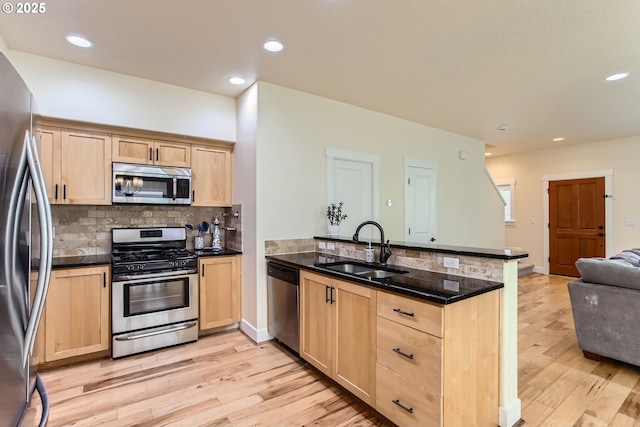 kitchen with appliances with stainless steel finishes, a sink, light brown cabinets, a peninsula, and open floor plan