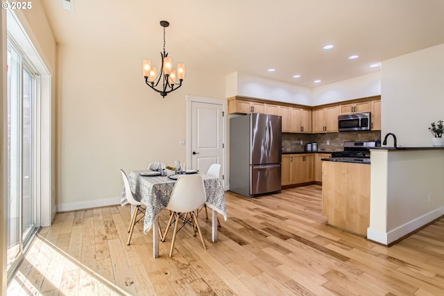 kitchen with dark countertops, an inviting chandelier, light wood-style floors, stainless steel appliances, and decorative backsplash