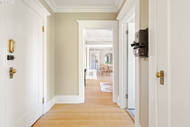 hall with baseboards, ornamental molding, and light wood-type flooring
