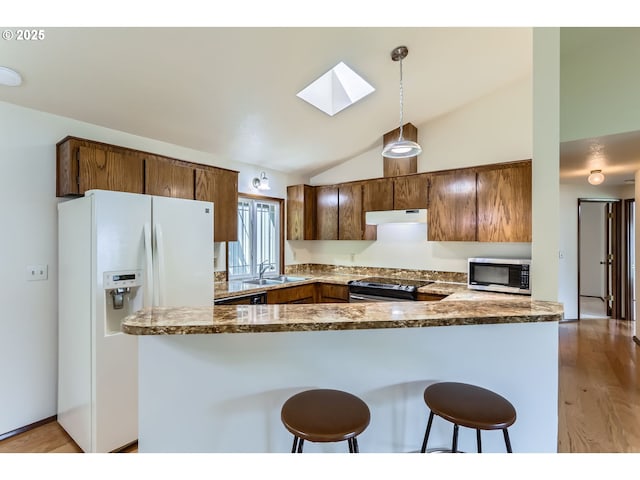 kitchen with a sink, vaulted ceiling with skylight, stainless steel appliances, a kitchen bar, and under cabinet range hood