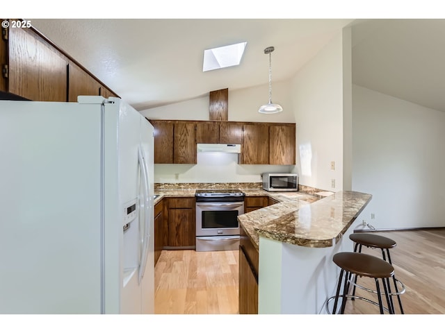kitchen with appliances with stainless steel finishes, a peninsula, lofted ceiling with skylight, under cabinet range hood, and light wood-style flooring