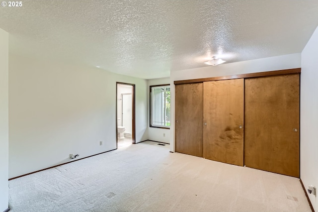 unfurnished bedroom featuring carpet flooring, connected bathroom, a textured ceiling, baseboards, and a closet