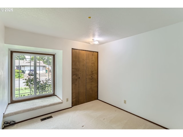 unfurnished bedroom with a closet, light colored carpet, a textured ceiling, and visible vents