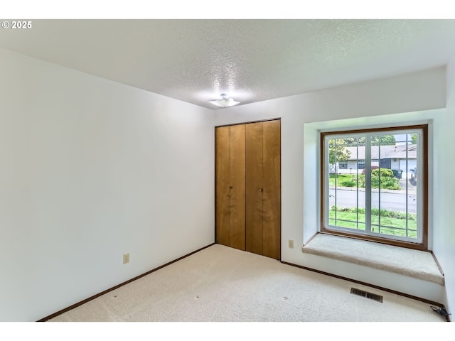 unfurnished bedroom with a textured ceiling, visible vents, baseboards, a closet, and carpet flooring