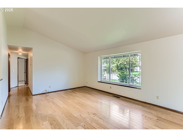 spare room with visible vents, light wood finished floors, baseboards, and vaulted ceiling