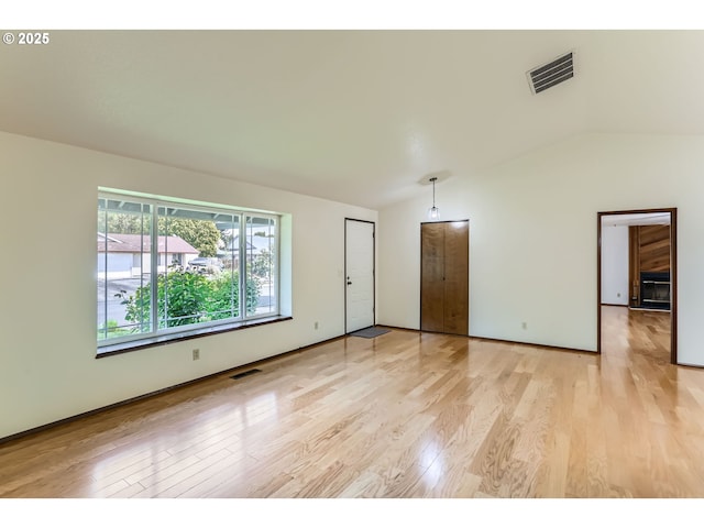empty room featuring vaulted ceiling, light wood-style flooring, and visible vents