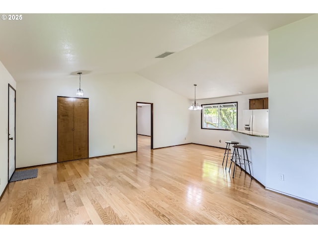 unfurnished living room featuring an inviting chandelier, vaulted ceiling, light wood-type flooring, and visible vents