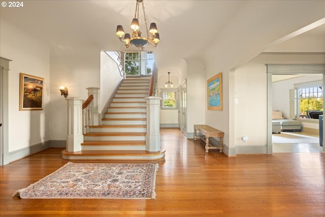 stairway with an inviting chandelier, a wealth of natural light, and hardwood / wood-style floors