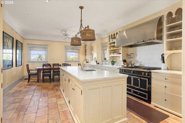 kitchen featuring range with two ovens, wall chimney exhaust hood, pendant lighting, decorative backsplash, and a kitchen island with sink