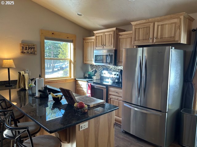 kitchen with light brown cabinetry, tasteful backsplash, appliances with stainless steel finishes, a breakfast bar area, and lofted ceiling