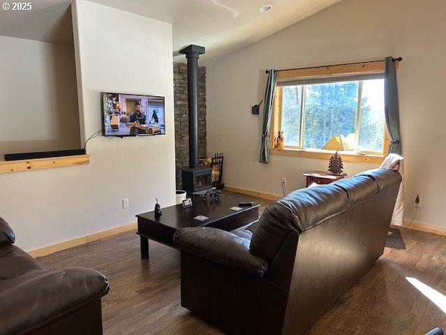 living room with vaulted ceiling, a wood stove, wood finished floors, and baseboards