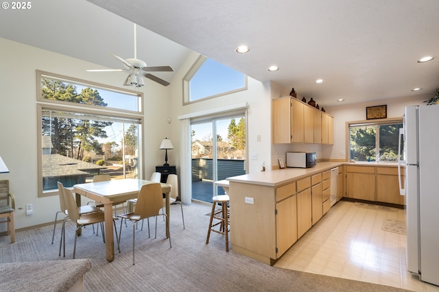 kitchen featuring lofted ceiling, white appliances, a breakfast bar area, kitchen peninsula, and light brown cabinets