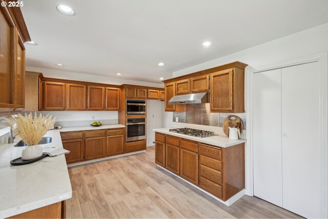 950 NW 161st Ter, Beaverton, OR 97006 - kitchen with brown cabinetry, appliances with stainless steel finishes, light countertops, under cabinet range hood, and recessed lighting