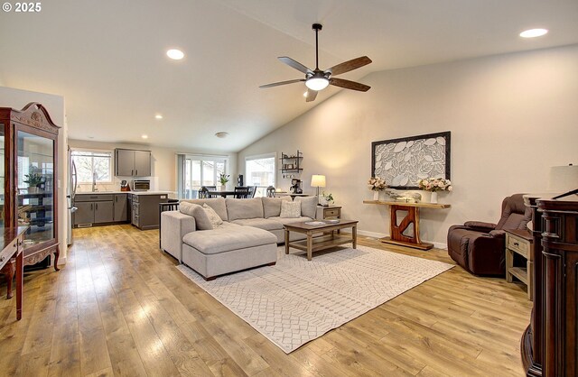 living area with recessed lighting, high vaulted ceiling, baseboards, ceiling fan, and light wood-style flooring