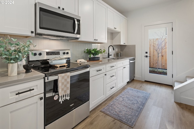 kitchen featuring sink, light wood-type flooring, appliances with stainless steel finishes, white cabinets, and backsplash