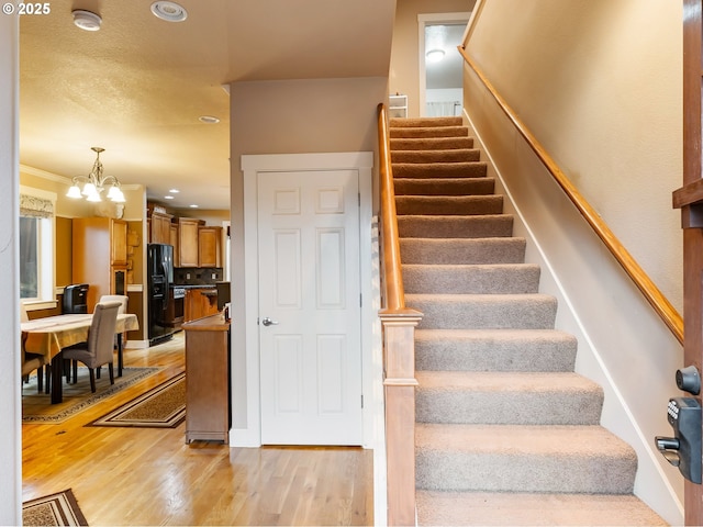 staircase with wood-type flooring, crown molding, and a notable chandelier