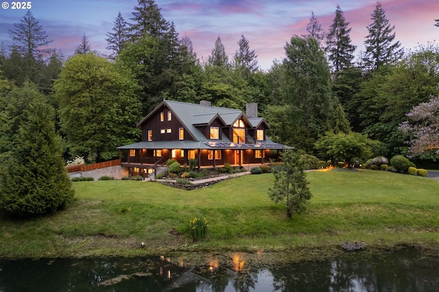 back of property featuring a chimney, a standing seam roof, a yard, metal roof, and a water view