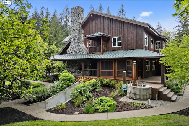 rear view of property featuring covered porch, a standing seam roof, a chimney, and metal roof