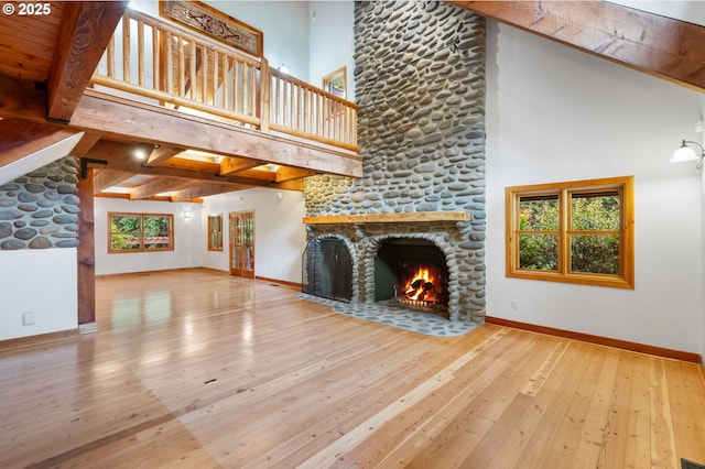 unfurnished living room featuring a stone fireplace, high vaulted ceiling, hardwood / wood-style floors, baseboards, and beamed ceiling