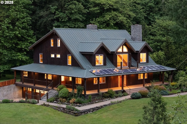 rear view of property featuring a chimney, a standing seam roof, metal roof, and a lawn