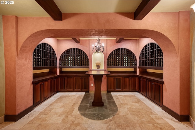 wine cellar featuring beamed ceiling, a textured wall, a chandelier, and light stone finish floors