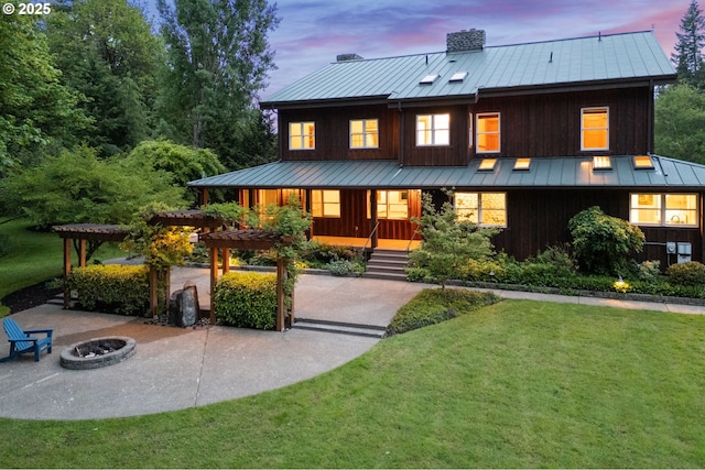 view of front of home with a standing seam roof, metal roof, a front yard, an outdoor fire pit, and a pergola