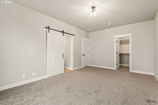 unfurnished bedroom featuring carpet flooring, a barn door, a spacious closet, a textured ceiling, and a closet