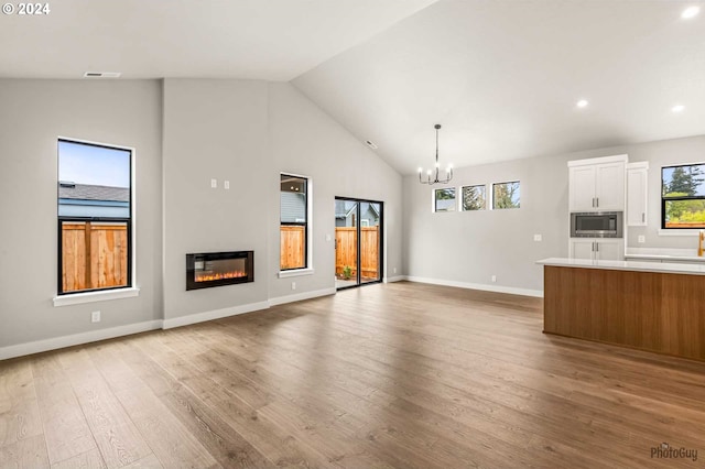 unfurnished living room with a chandelier, high vaulted ceiling, a healthy amount of sunlight, and light wood-type flooring