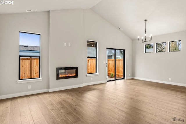 unfurnished living room with a notable chandelier, light wood-type flooring, and high vaulted ceiling