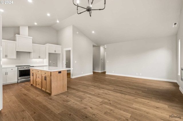 kitchen with stainless steel range, an inviting chandelier, high vaulted ceiling, a center island, and white cabinetry