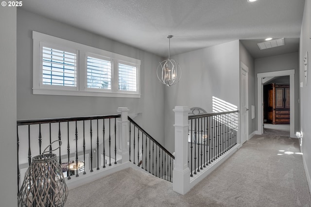 hallway featuring a textured ceiling, light carpet, and a chandelier