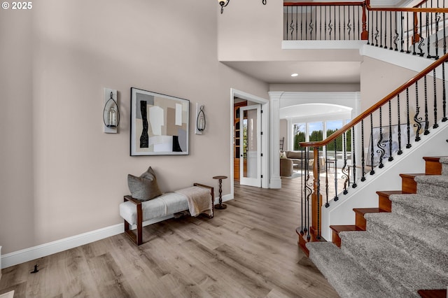 foyer entrance with a towering ceiling, stairway, baseboards, and wood finished floors