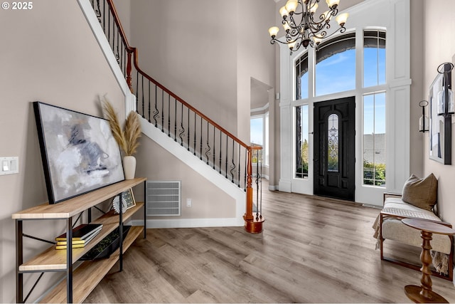 entrance foyer featuring visible vents, wood finished floors, baseboards, a towering ceiling, and stairs