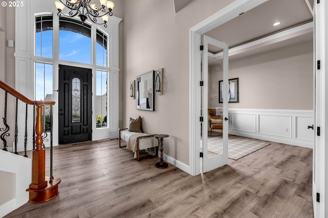 foyer featuring stairway, light wood-type flooring, a high ceiling, an inviting chandelier, and a decorative wall