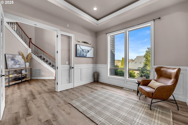 living area featuring visible vents, a tray ceiling, stairs, wainscoting, and light wood-type flooring