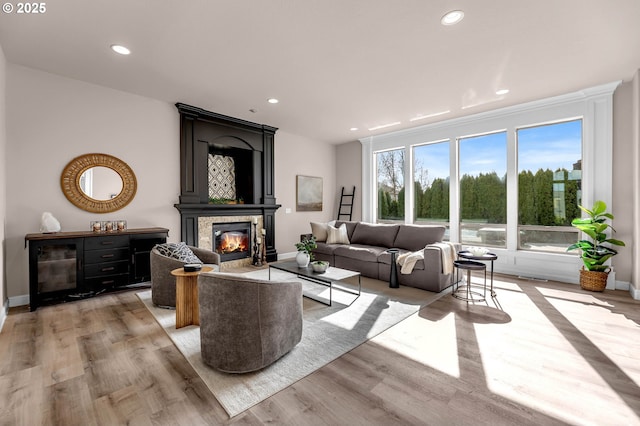 living area featuring a glass covered fireplace, recessed lighting, light wood-type flooring, and baseboards