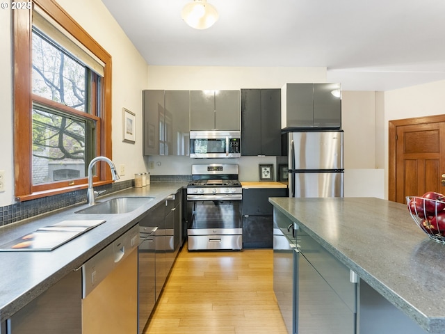 kitchen with appliances with stainless steel finishes, light wood-type flooring, a sink, and gray cabinetry